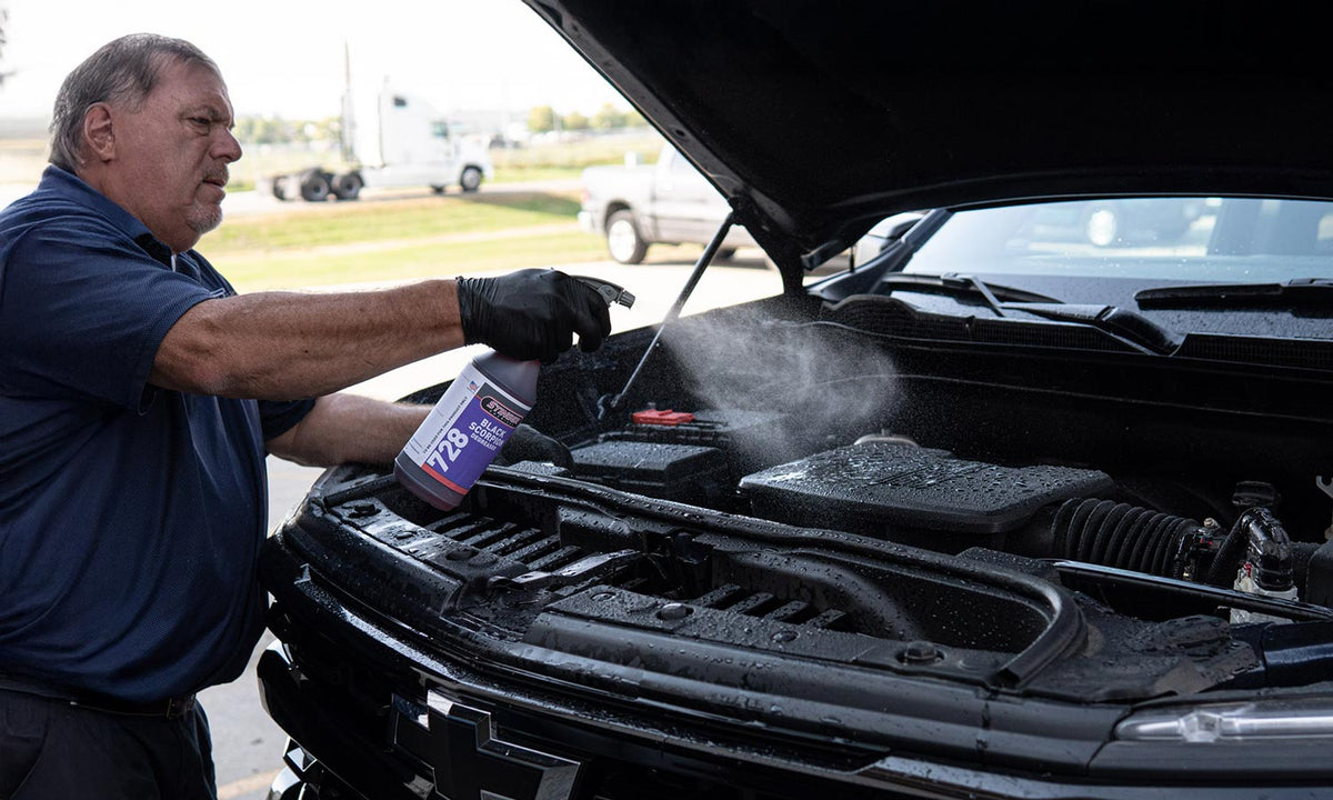 Shane spraying black scorpion degreaser on a truck's engine bay