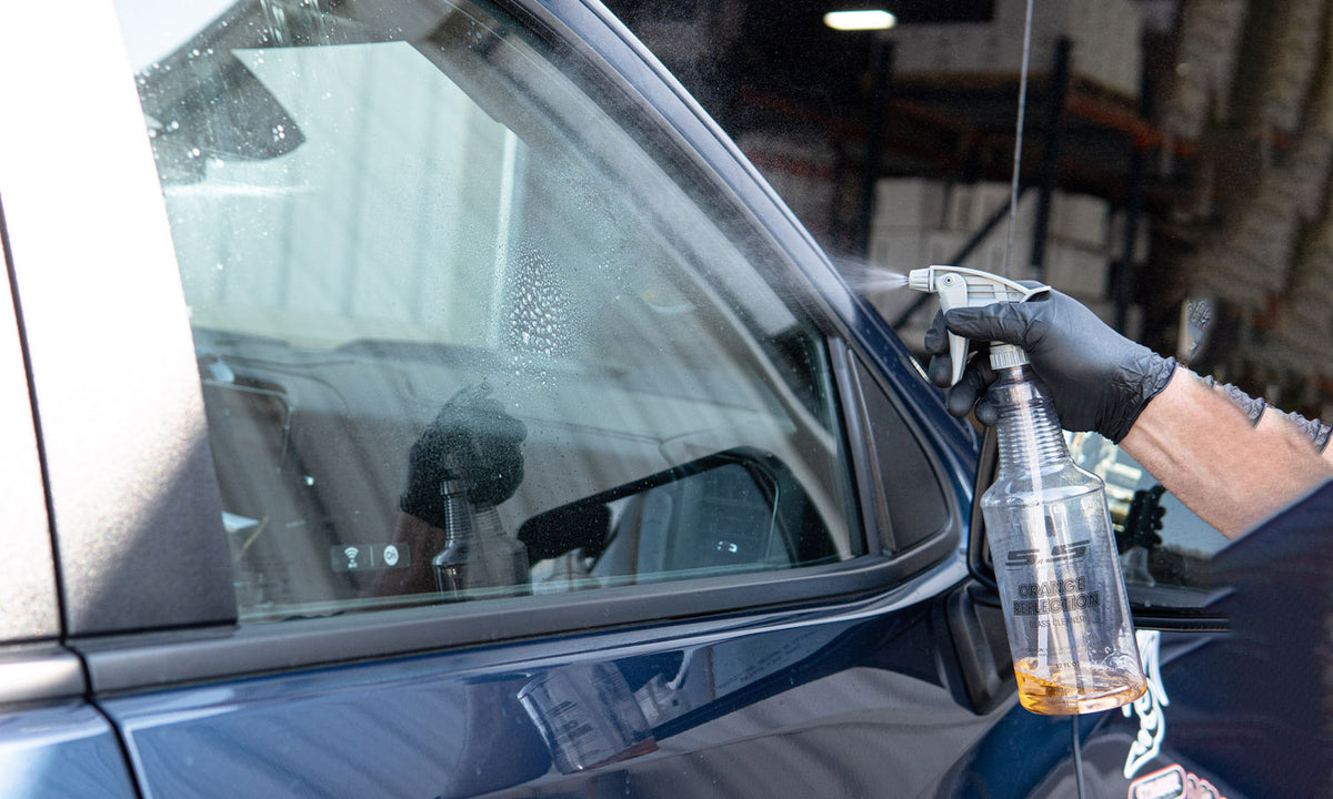 cleaning glass with a near-empty bottle of orange reflection glass cleaner on a truck outside in the sunlight