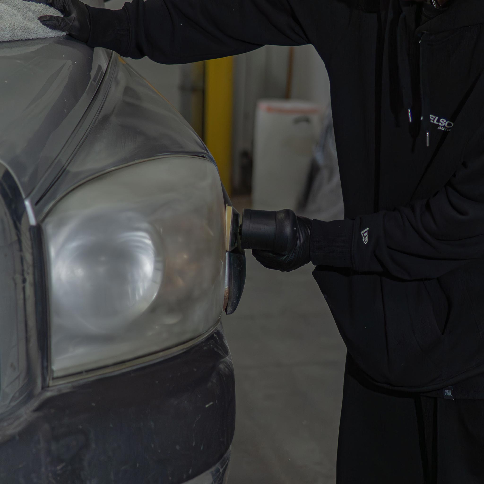 Person sanding a car headlight in a garage setting