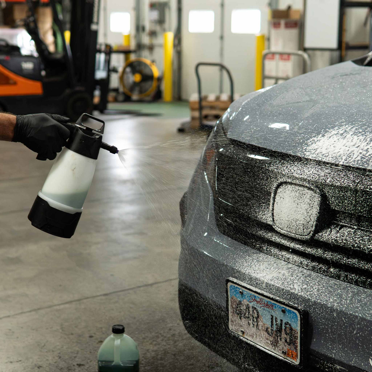 Stinger Chemical Ultimate Wash-N-Wax 714 foam sprayed onto the front of a gray SUV in a shop