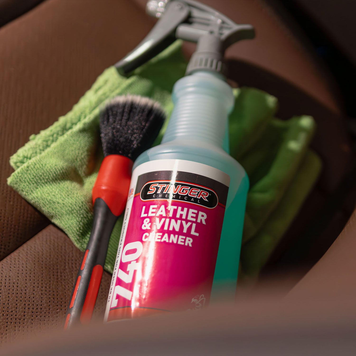 Stinger leather and vinyl cleaner with cleaning tools on a brown leather surface