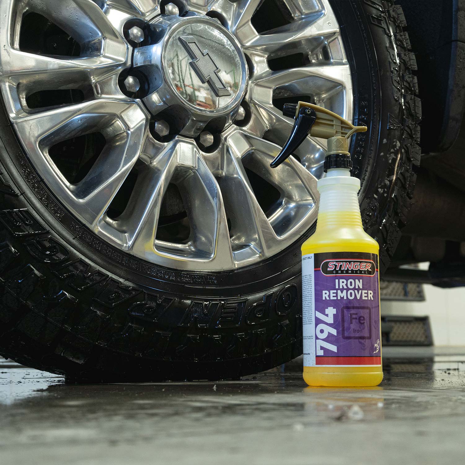 Spray bottle of Stinger Iron Remover next to a car tire with a shiny rim.