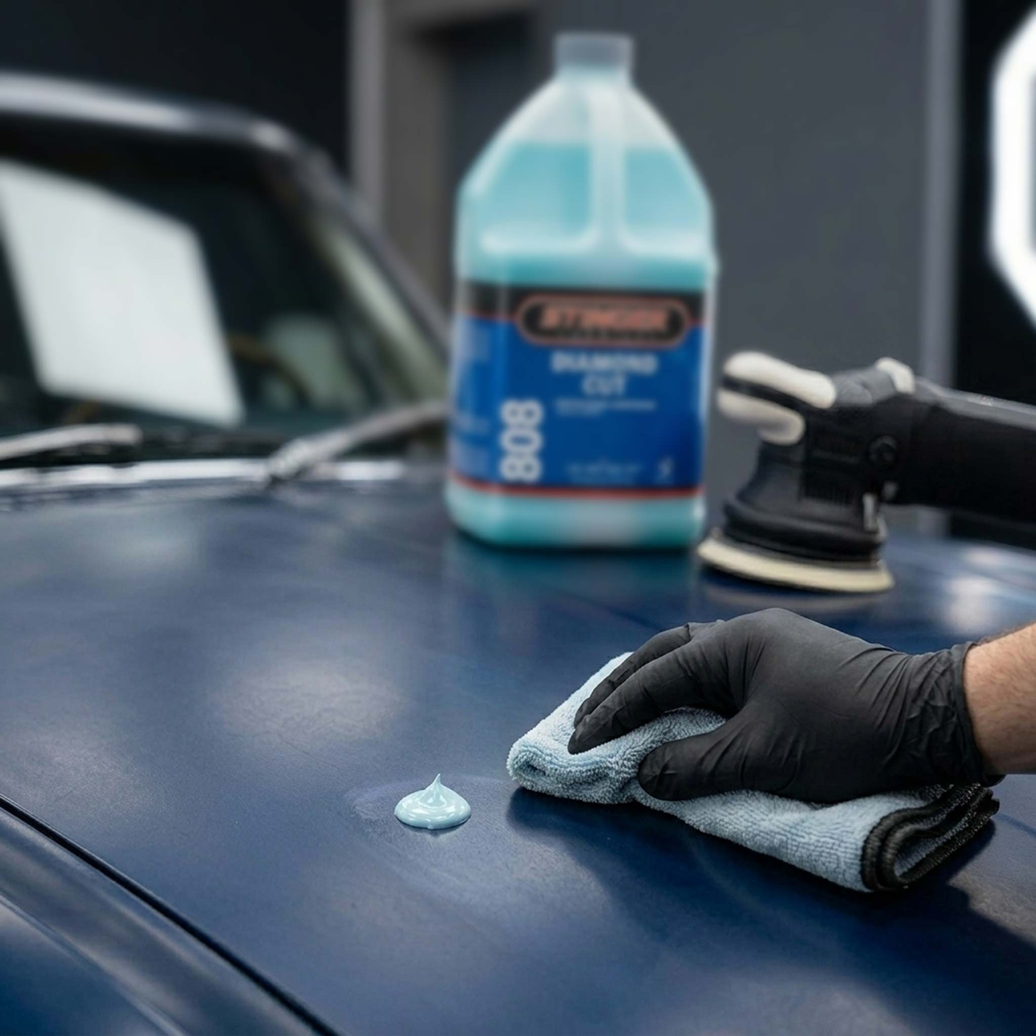 Person applying blue diamond cut to a car's surface with a bottle in the background.