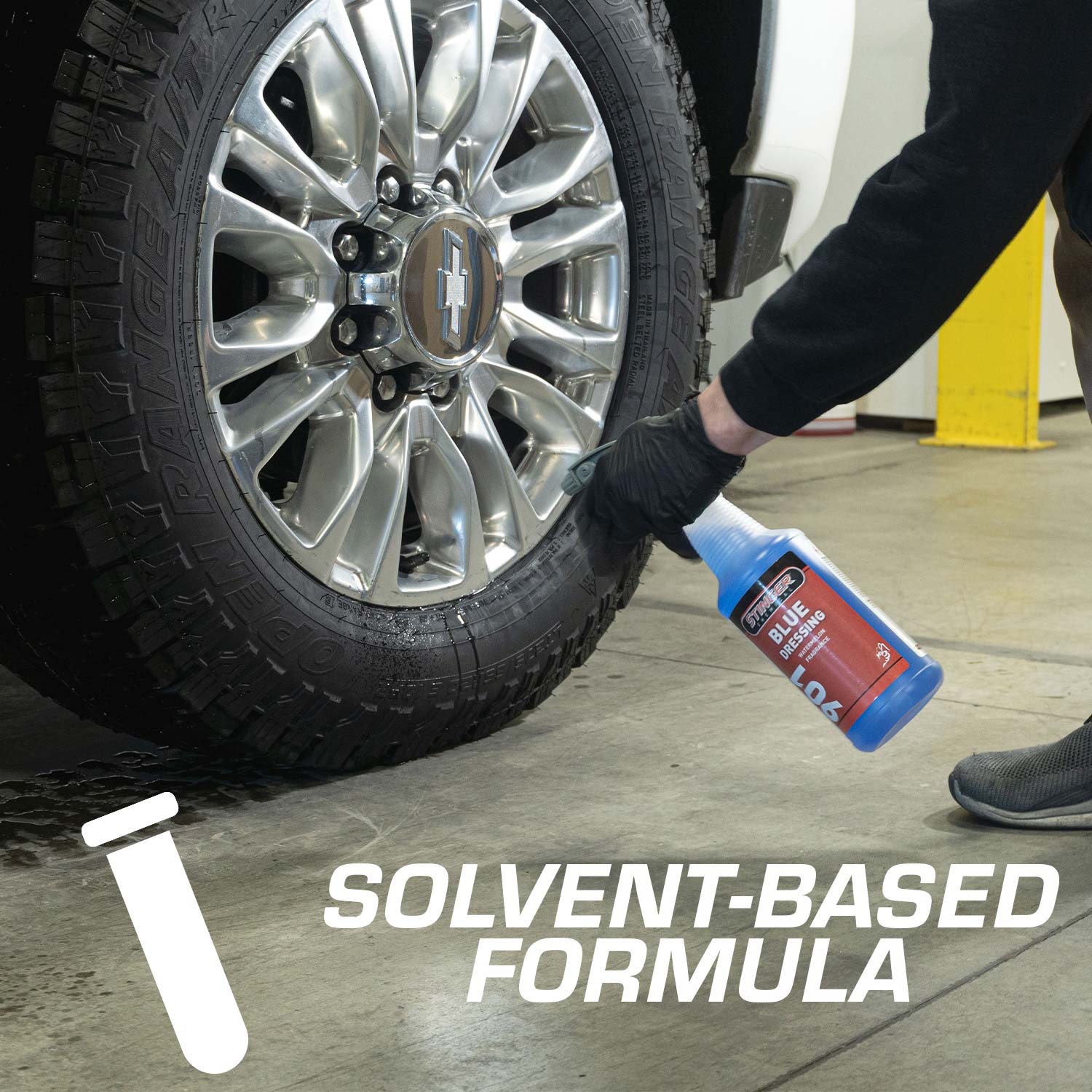 Person applying a solvent-based formula to a car tire with a bottle, in a garage setting.