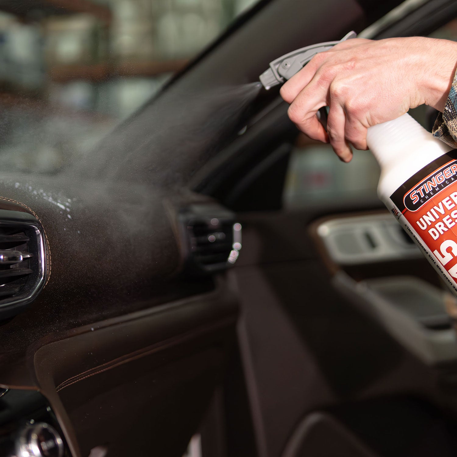 Person cleaning car interior with a spray bottle labeled 'Stinger Universal Dressing'.