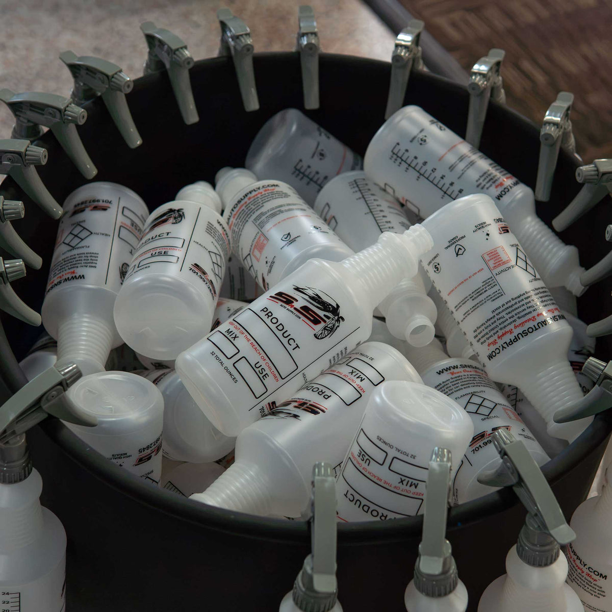 SNS Auto Supply printed 32 oz spray bottles D02 piled in a bin with gray trigger sprayers on the rim