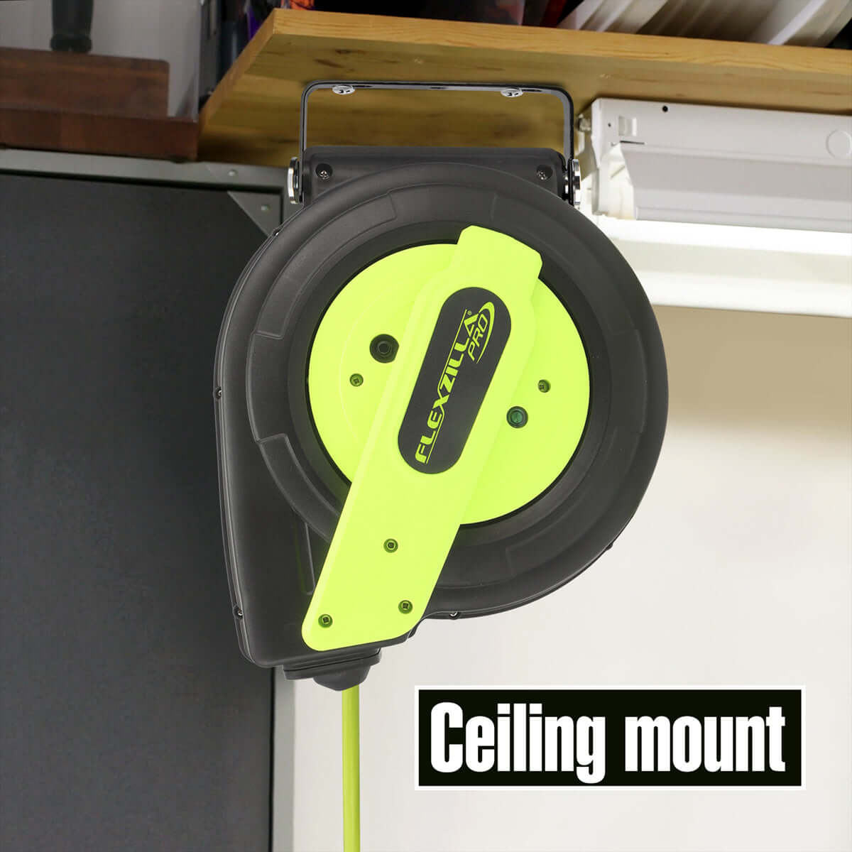 Green extension cord reel with 'Flexzilla' branding on a ceiling mount, attached to a wooden surface.