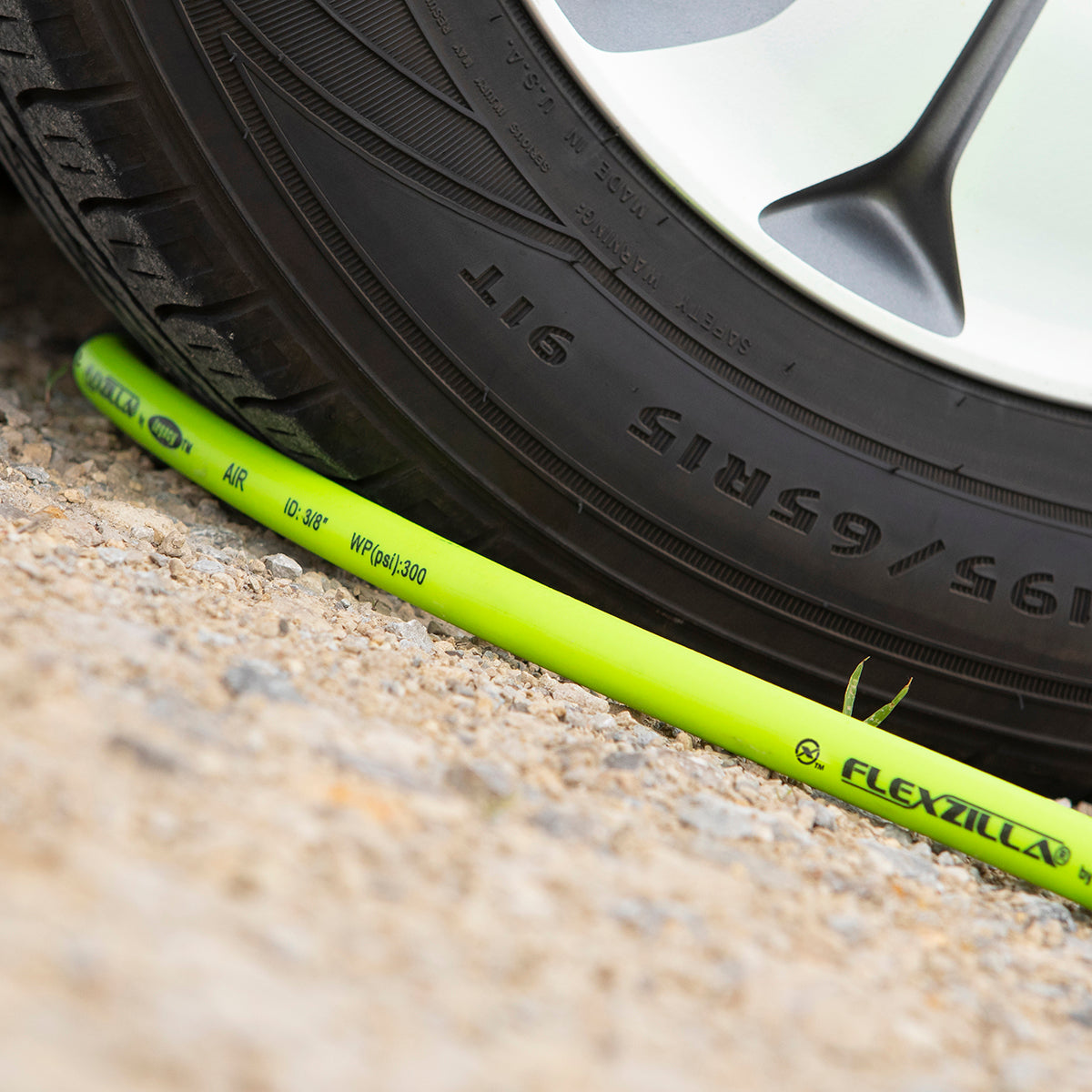 Green air hose next to a car tire on a gravel surface