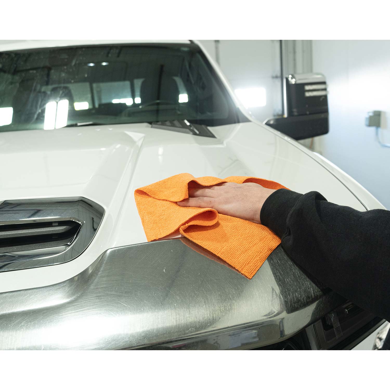 Person cleaning a car's hood with an orange microfiber towel