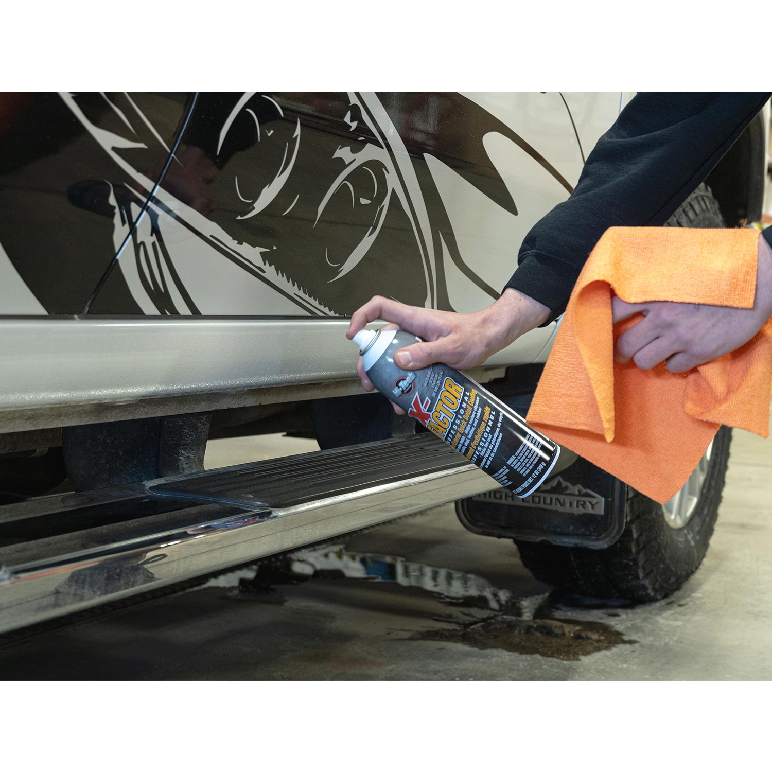 Person cleaning a car with a spray can and orange towel
