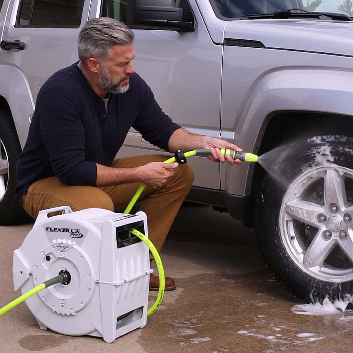Man using a pressure washer attached to a Flexzilla reel while washing a car.