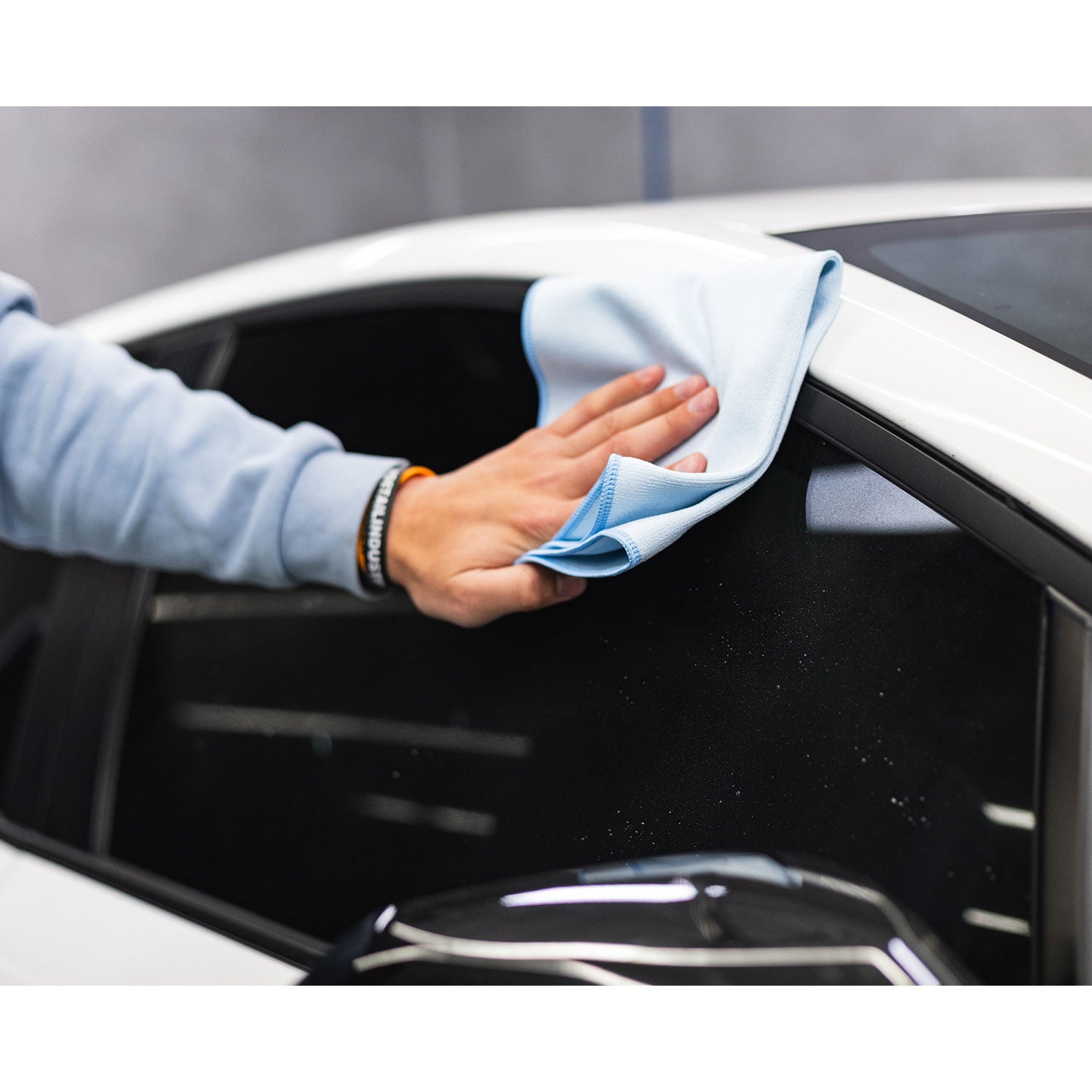 Person cleaning a car window with a blue microfiber cloth