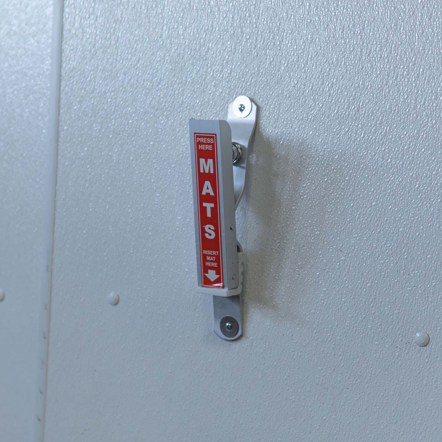 Metallic floor mat clamp with red and white text on a light gray wall