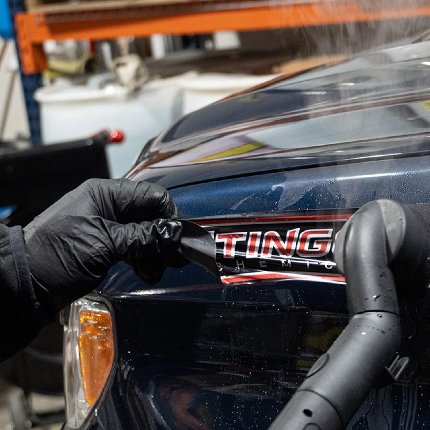 Person wearing black gloves adjusting a car sticker on a vehicle, with a blurred background.
