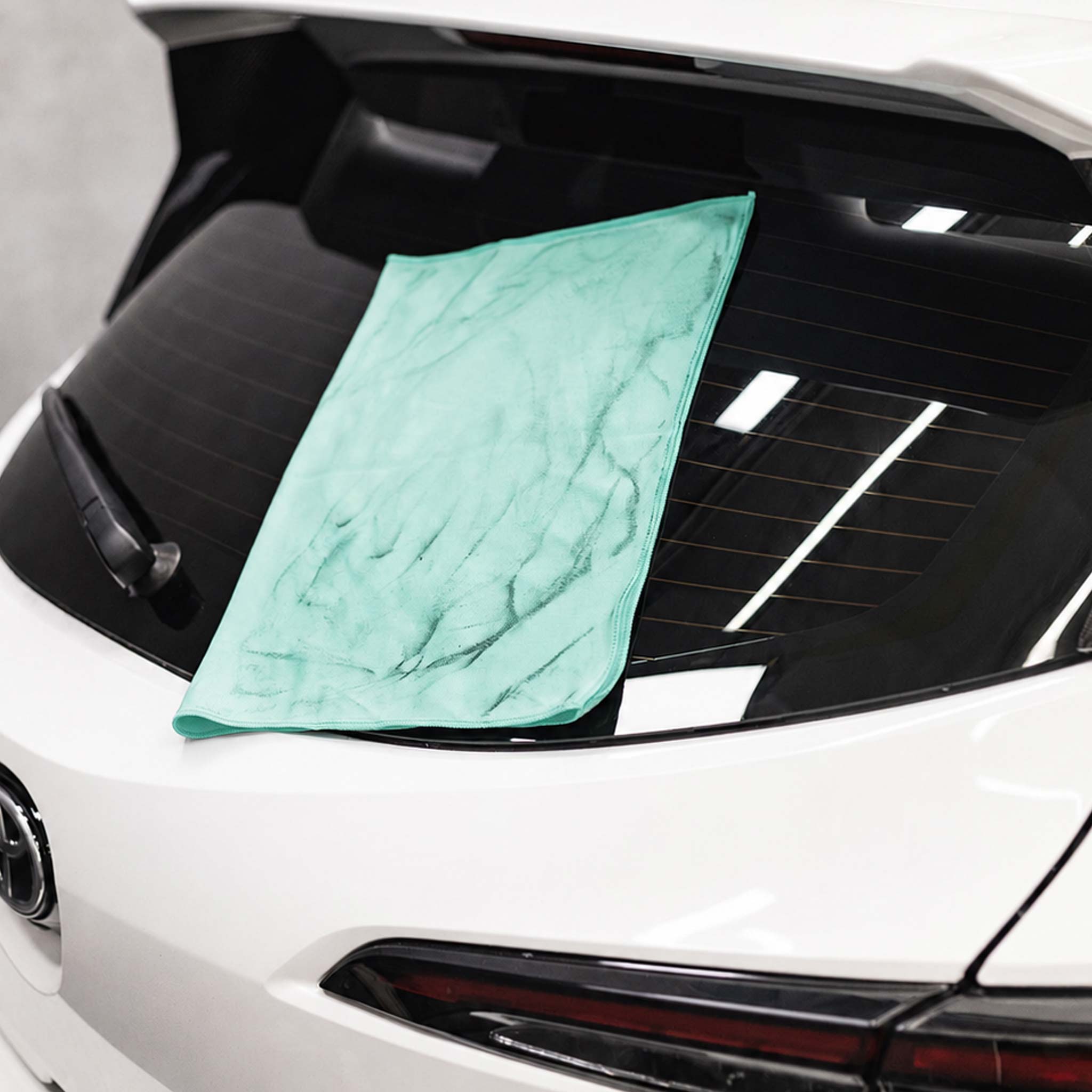 Green microfiber towel draped over a car's windshield with a white car in the background