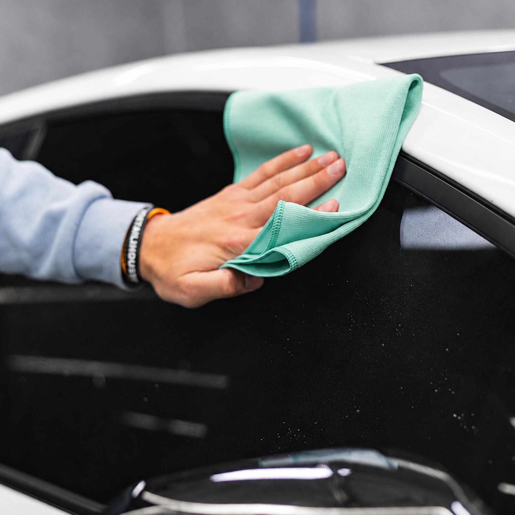 Person cleaning a car window with a green microfiber cloth