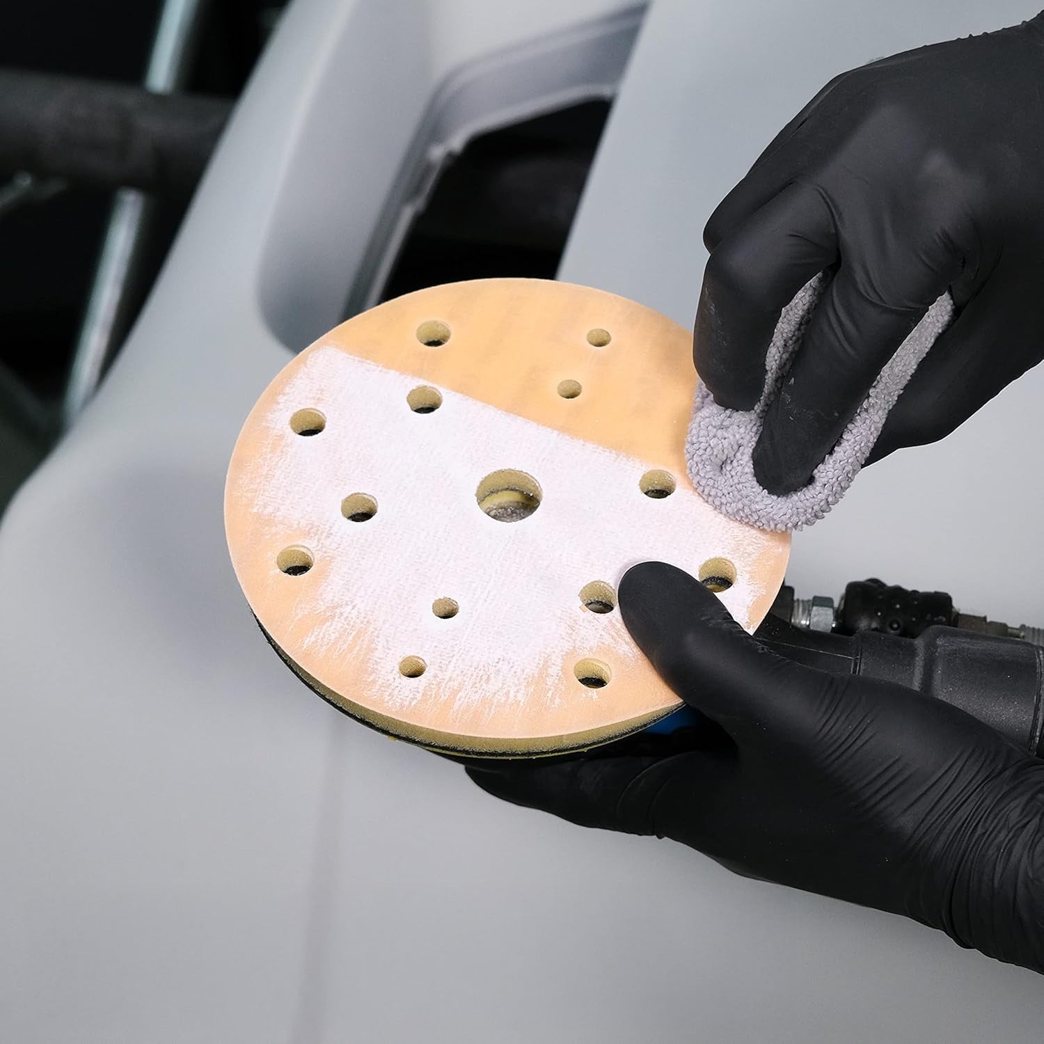 Person wearing black gloves holding and cleaning a sanding disc on a car surface