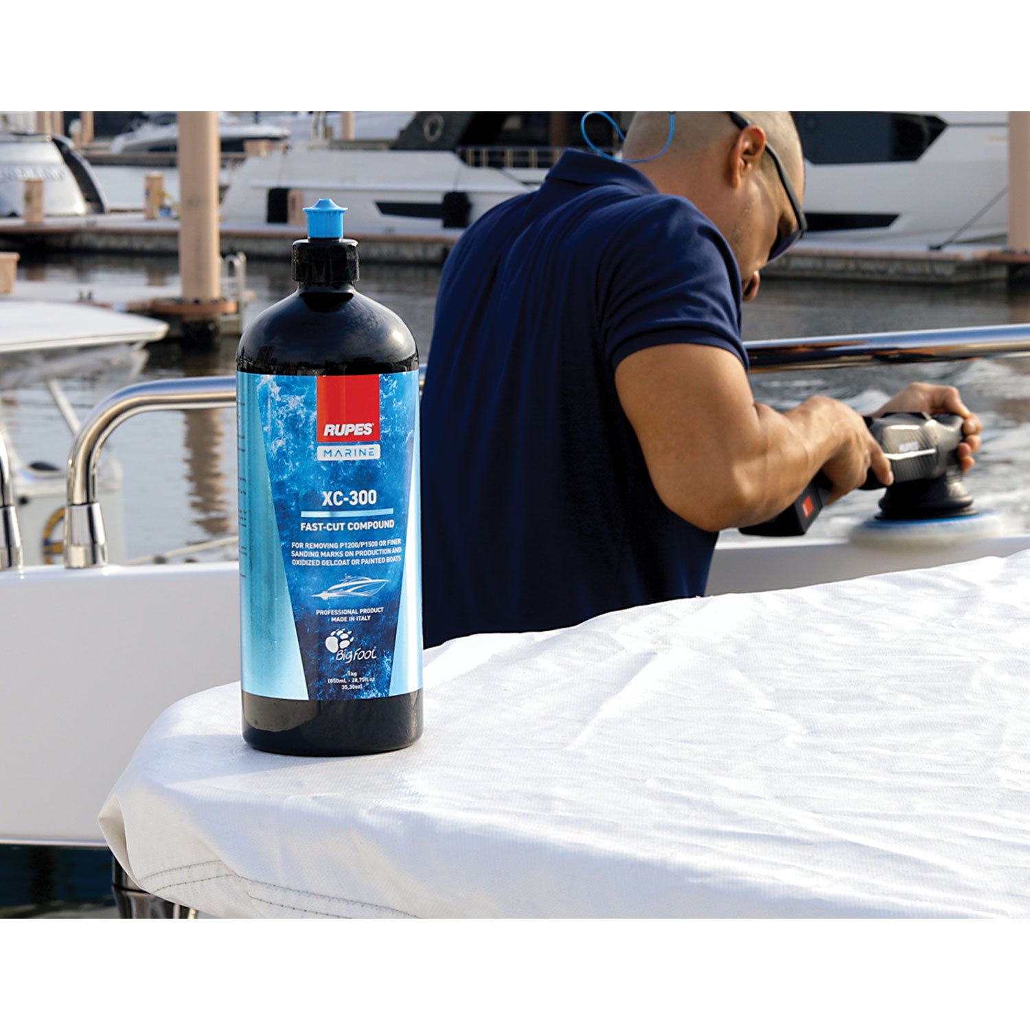 Person working on a boat with a bottle of Rupes XC-300 compound in the foreground.