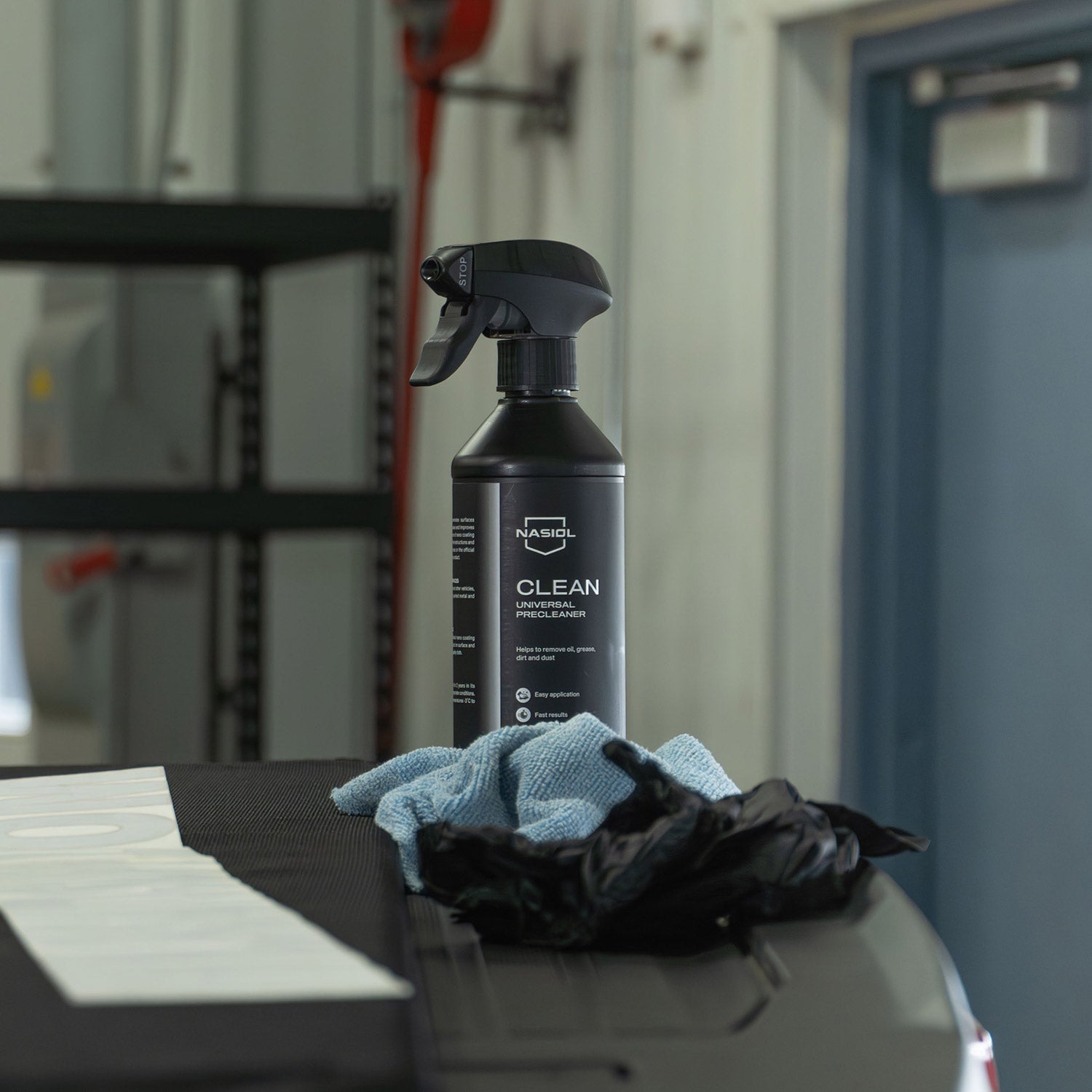 Spray bottle labeled 'Nashol Clean' with cloths on a car tonneau cover in a garage setting
