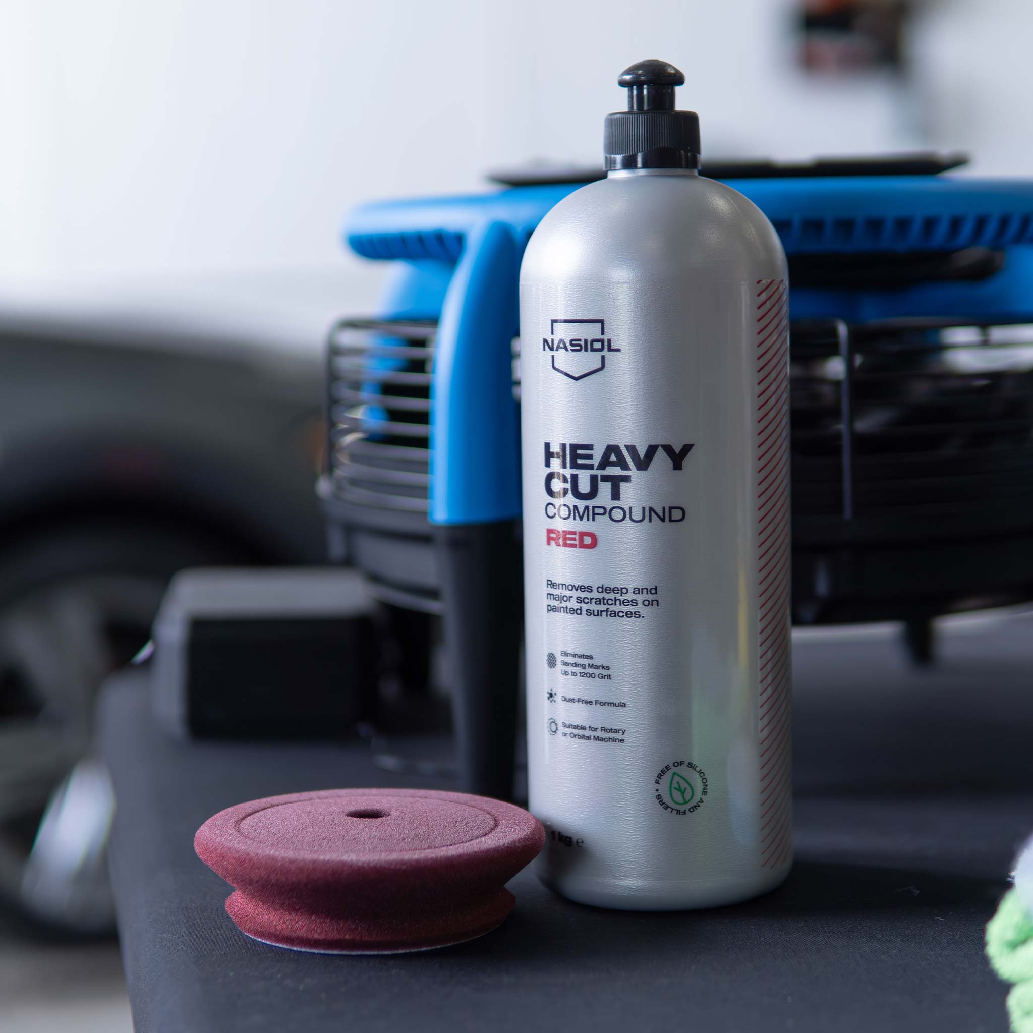 Car care product bottle labeled 'Heavy Cut Compound Red' with a maroon polishing pad on a table