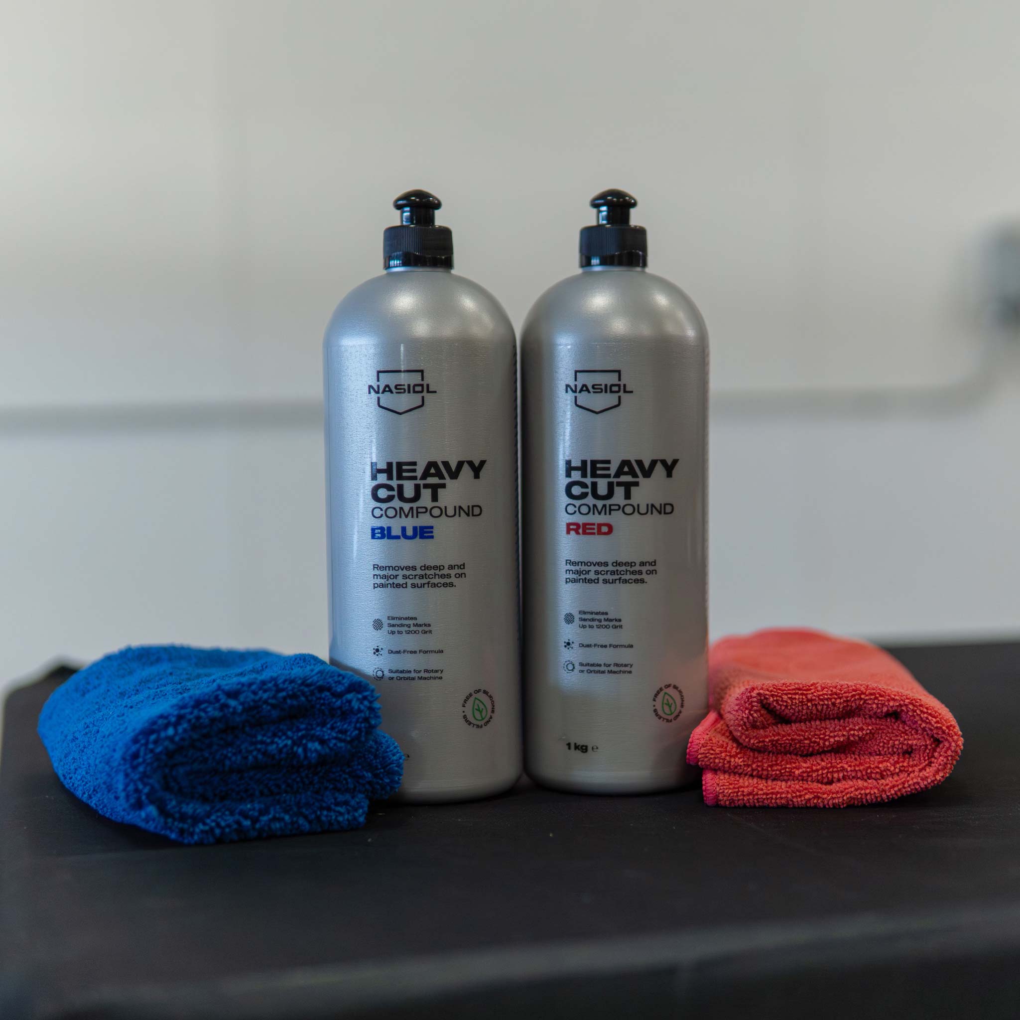 Two bottles of 'Heavy Cut Compound' by NASIOL with blue and red cloths on a black surface.