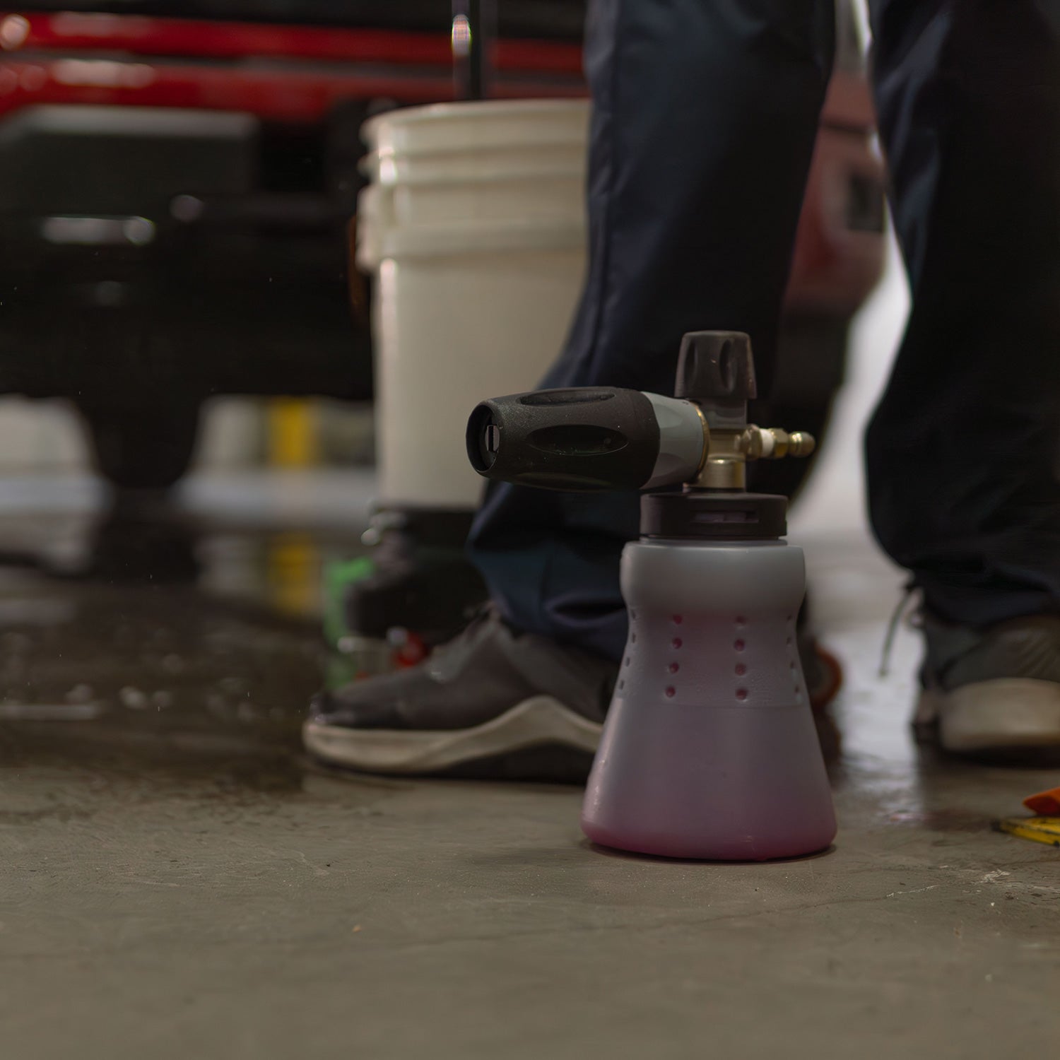 Pink foam cannon spray gun on a concrete floor with blurred legs and feet in the background