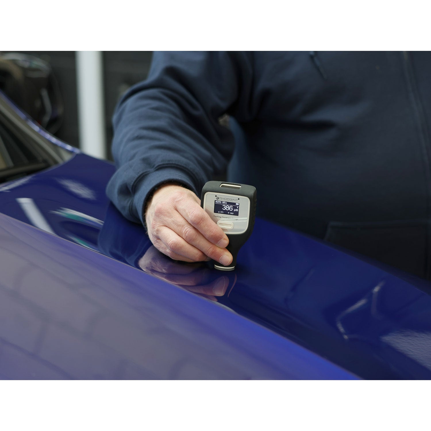 Someone using a coating thickness gauge on a blue truck hood