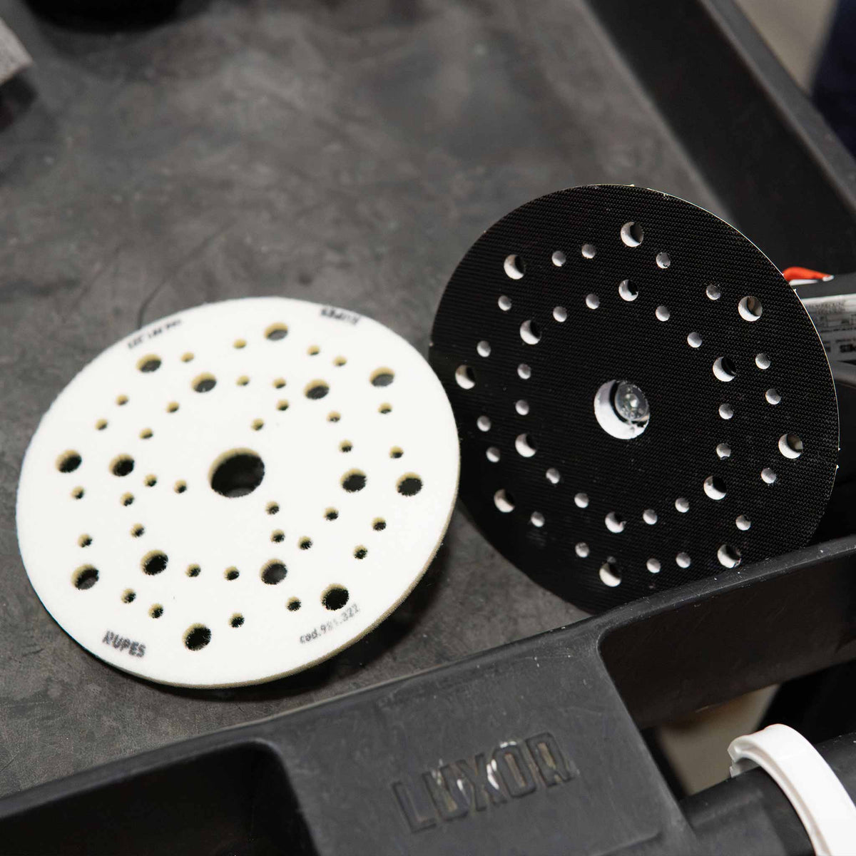RUPES 6 inch interface pad next to a multi hole sander backing plate on a cart