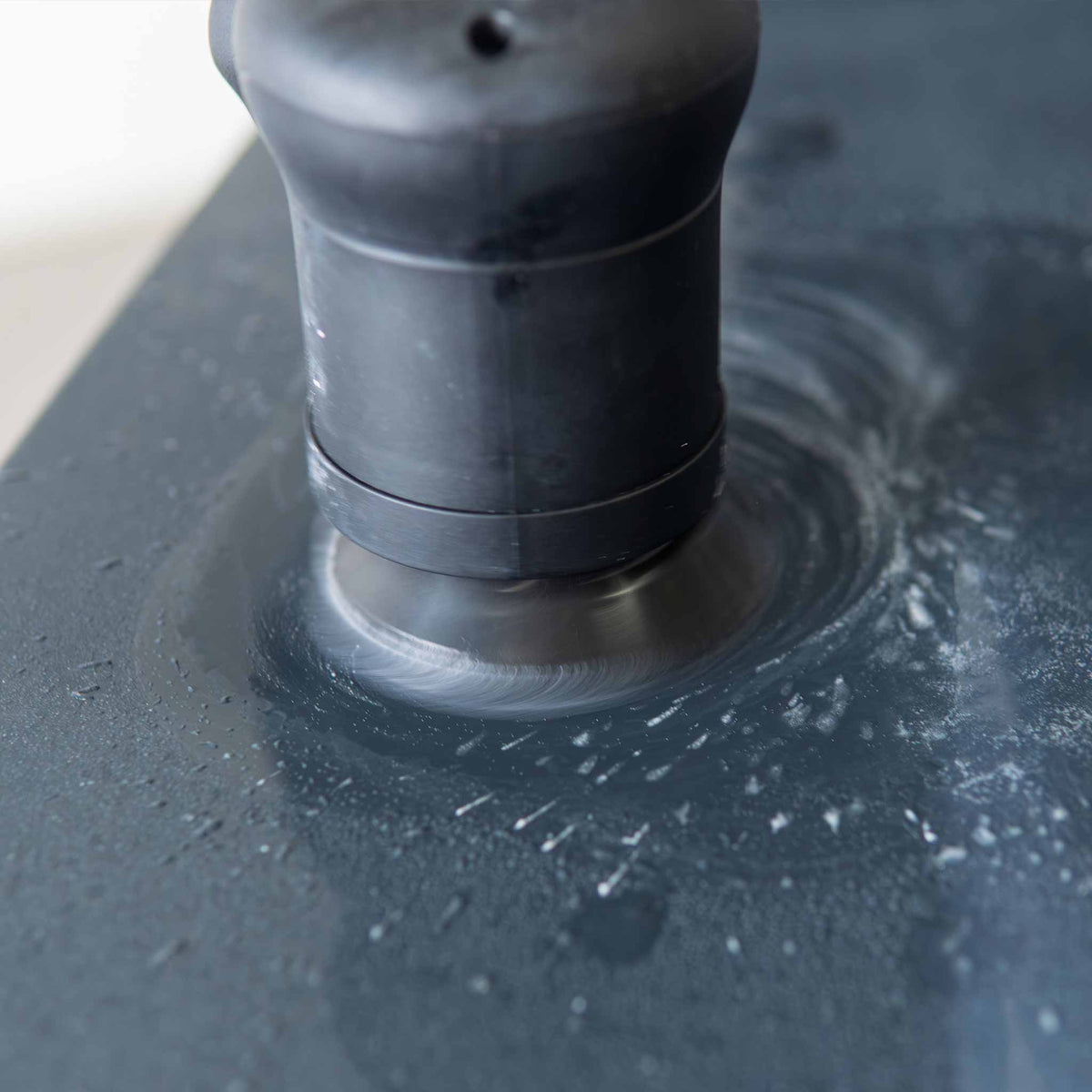 Mini sander wet sanding a black panel with water and slurry around the pad