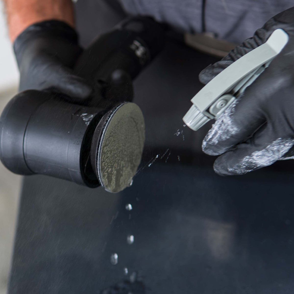 Spraying water onto a RUPES WetFinish disc before wet sanding a black panel