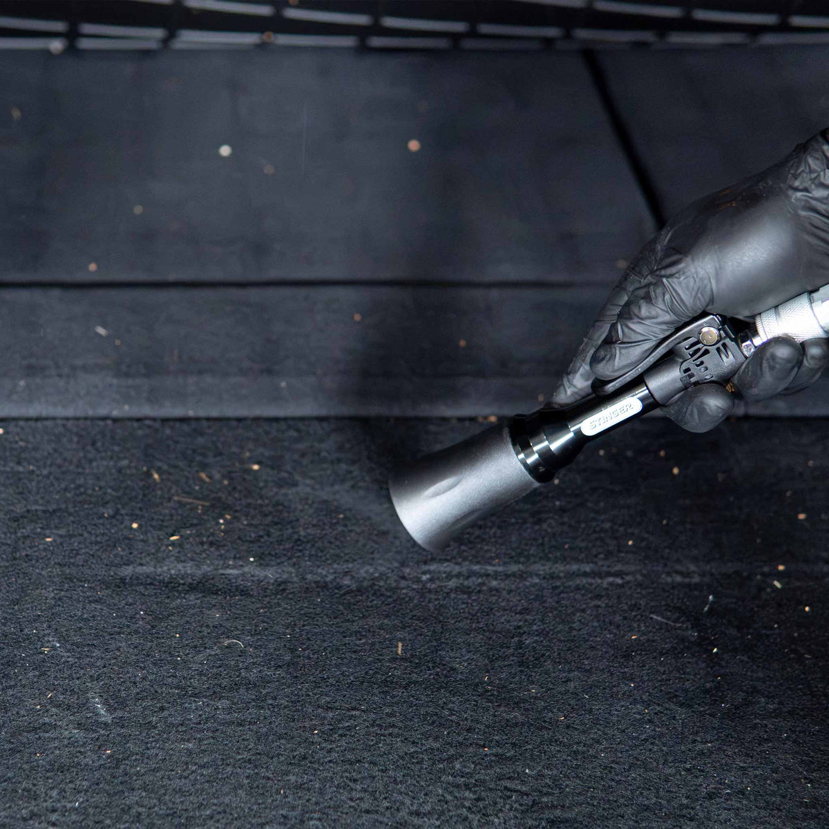 Stinger Twister Mini Blow Gun clearing dirt from the carpeted cargo area of a vehicle