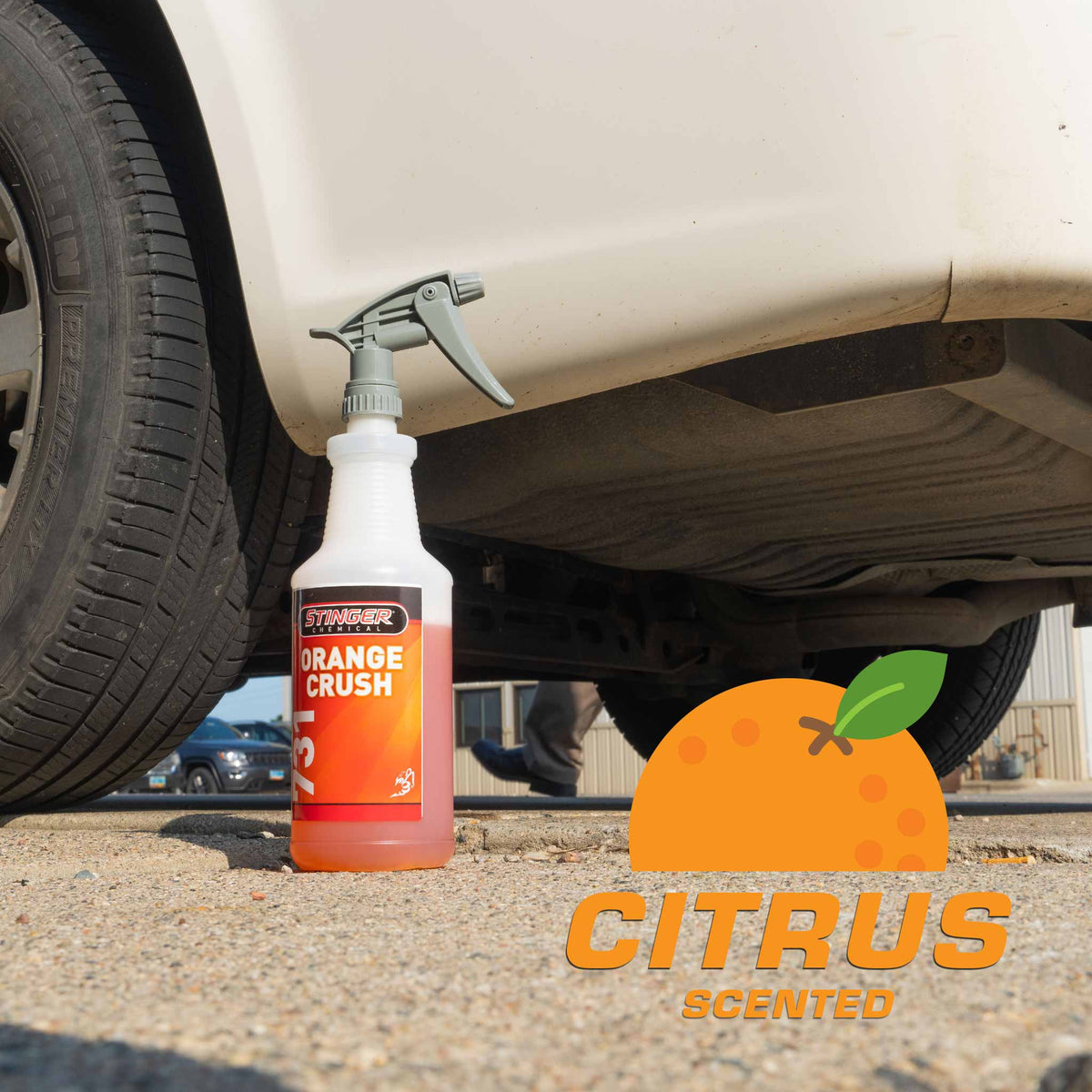 Stinger Chemical Orange Crush 731 citrus scented spray bottle on pavement beside a white vehicle's tire