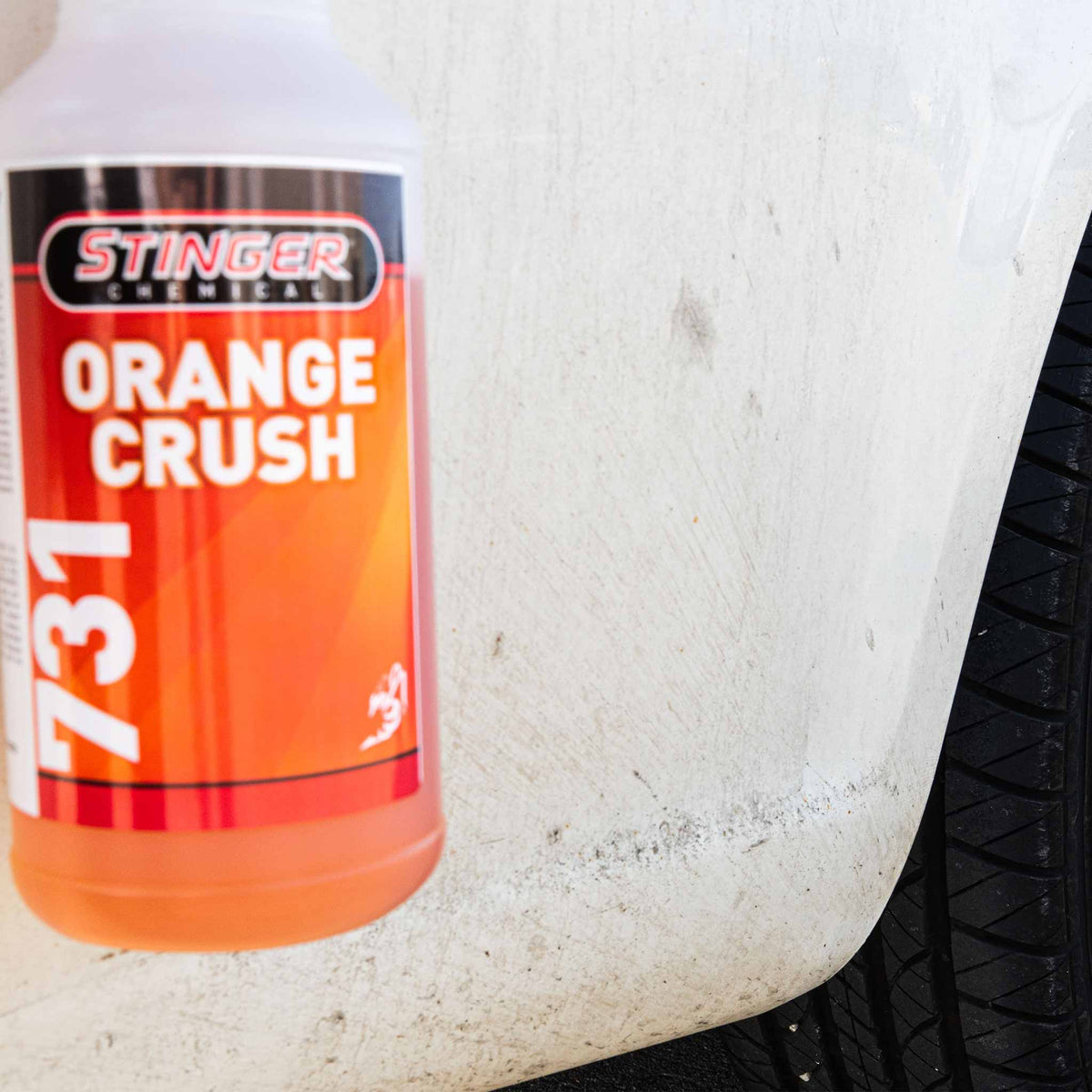 Stinger Chemical Orange Crush 731 spray bottle held against road grime on a white vehicle's lower panel