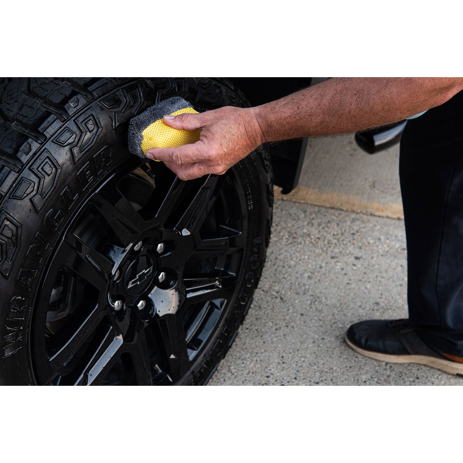 Person cleaning a black car wheel with a yellow sponge