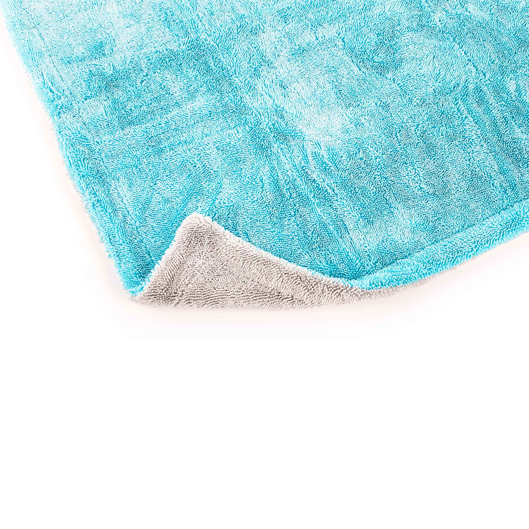 A close-up of a turquoise blue plush towel with a folded corner revealing a soft gray underside, set against a plain white background.
