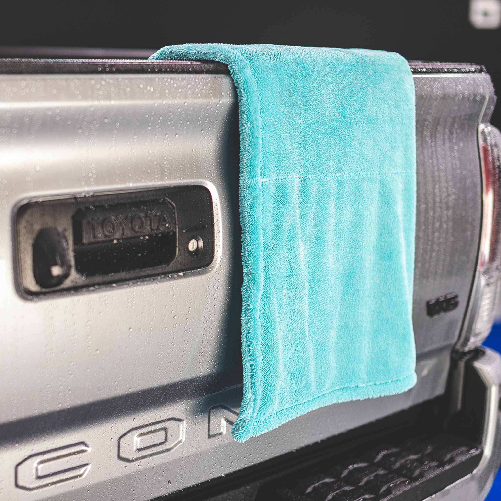 A turquoise microfiber cleaning cloth draped over the tailgate of a silver Toyota Tacoma truck.