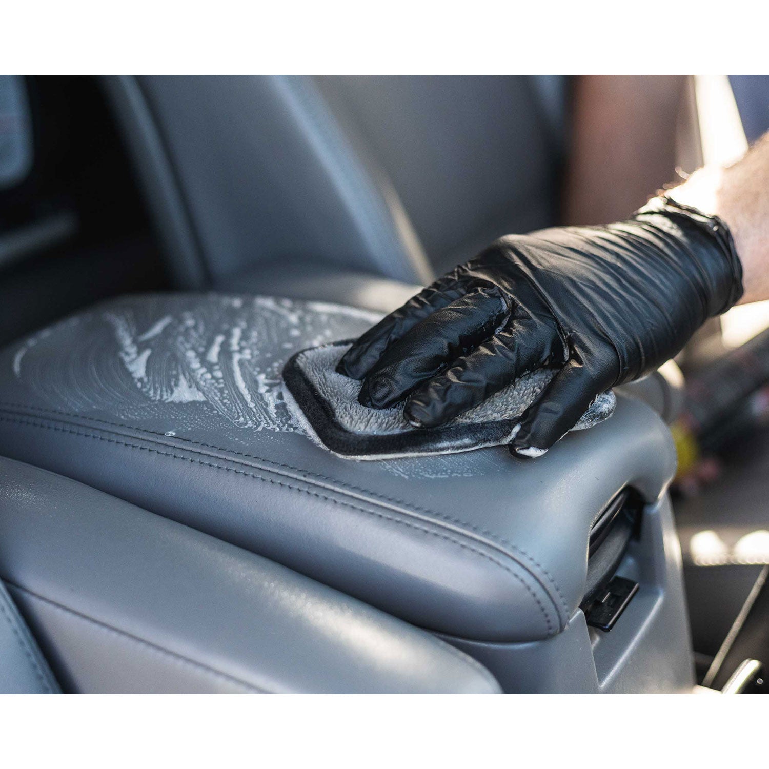 Person cleaning car interior console with a black glove and interior scrubber