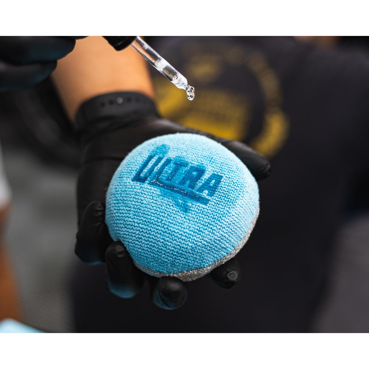 Blue and grey applicator ball with 'Ultra' branding held by a gloved hand with ceramic coating being poured on it