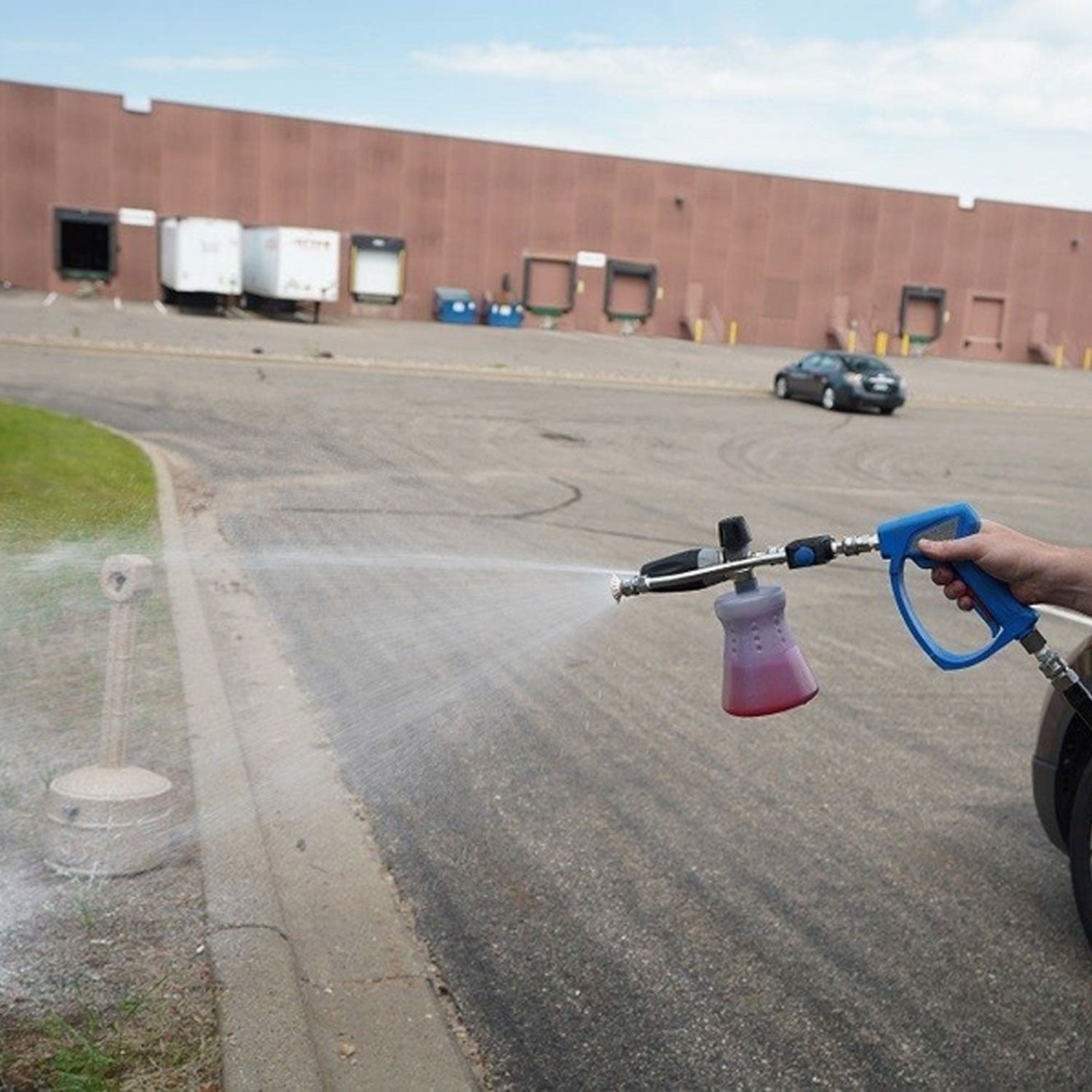 Person using a pressure washer with MTM Mezzo Valve to clean a driveway in front of a warehouse.