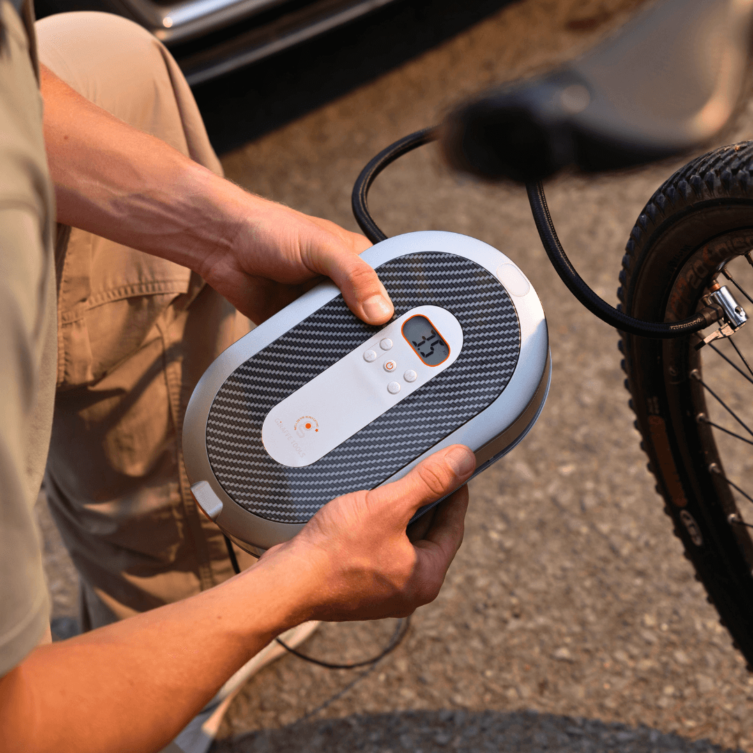 Person holding a portable air compressor next to a bicycle tire.
