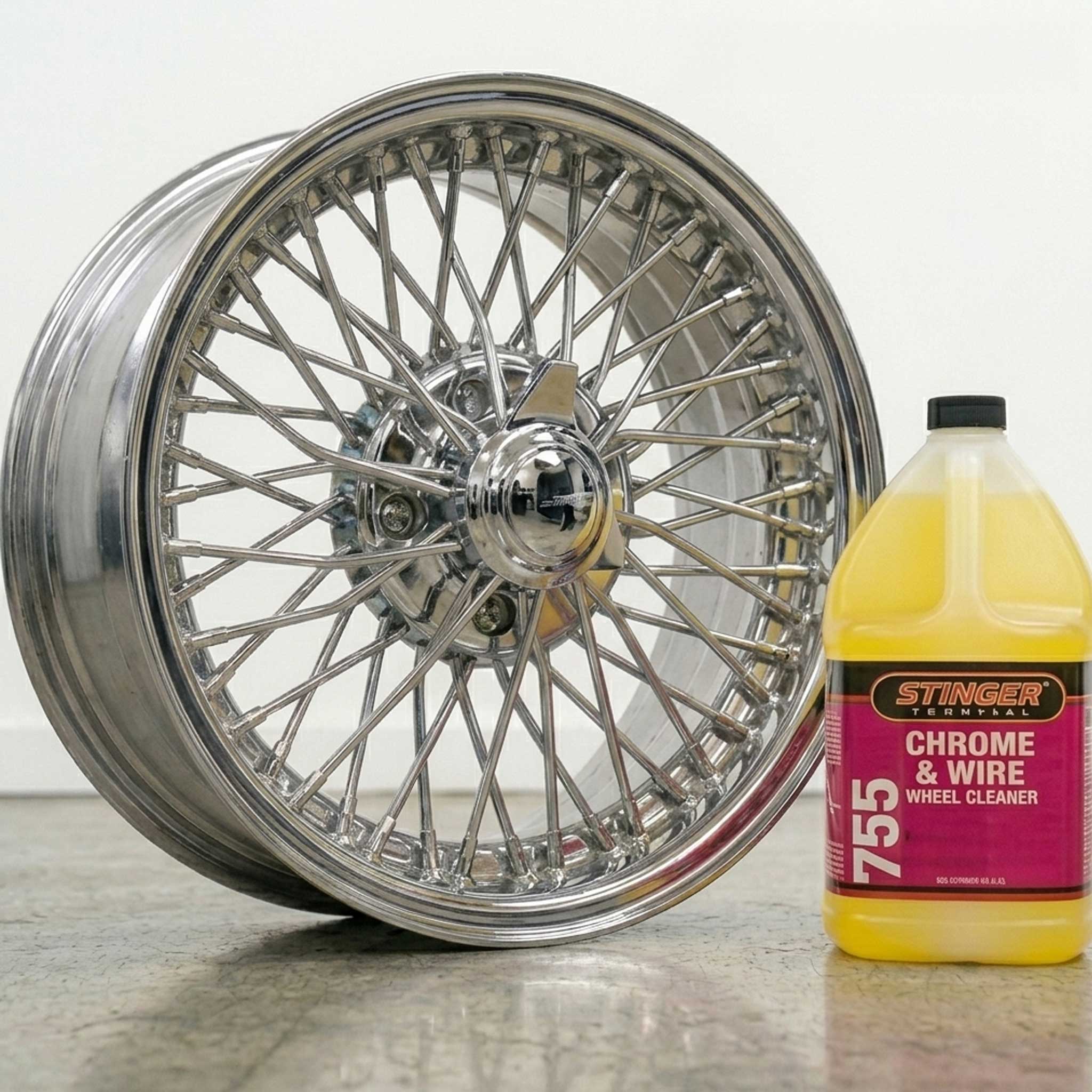 Chrome wheel and Stinger 755 Chrome & Wire Wheel Cleaner bottle on a reflective surface.