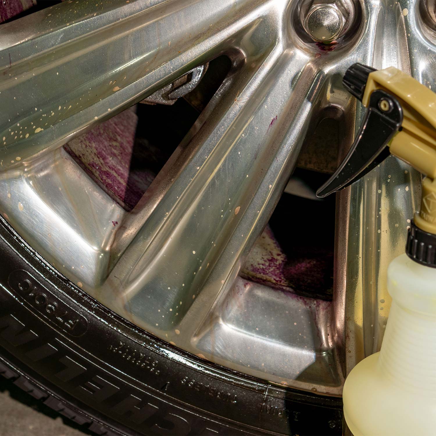 Car wheel being cleaned with a spray bottle showing purple iron remover reaction