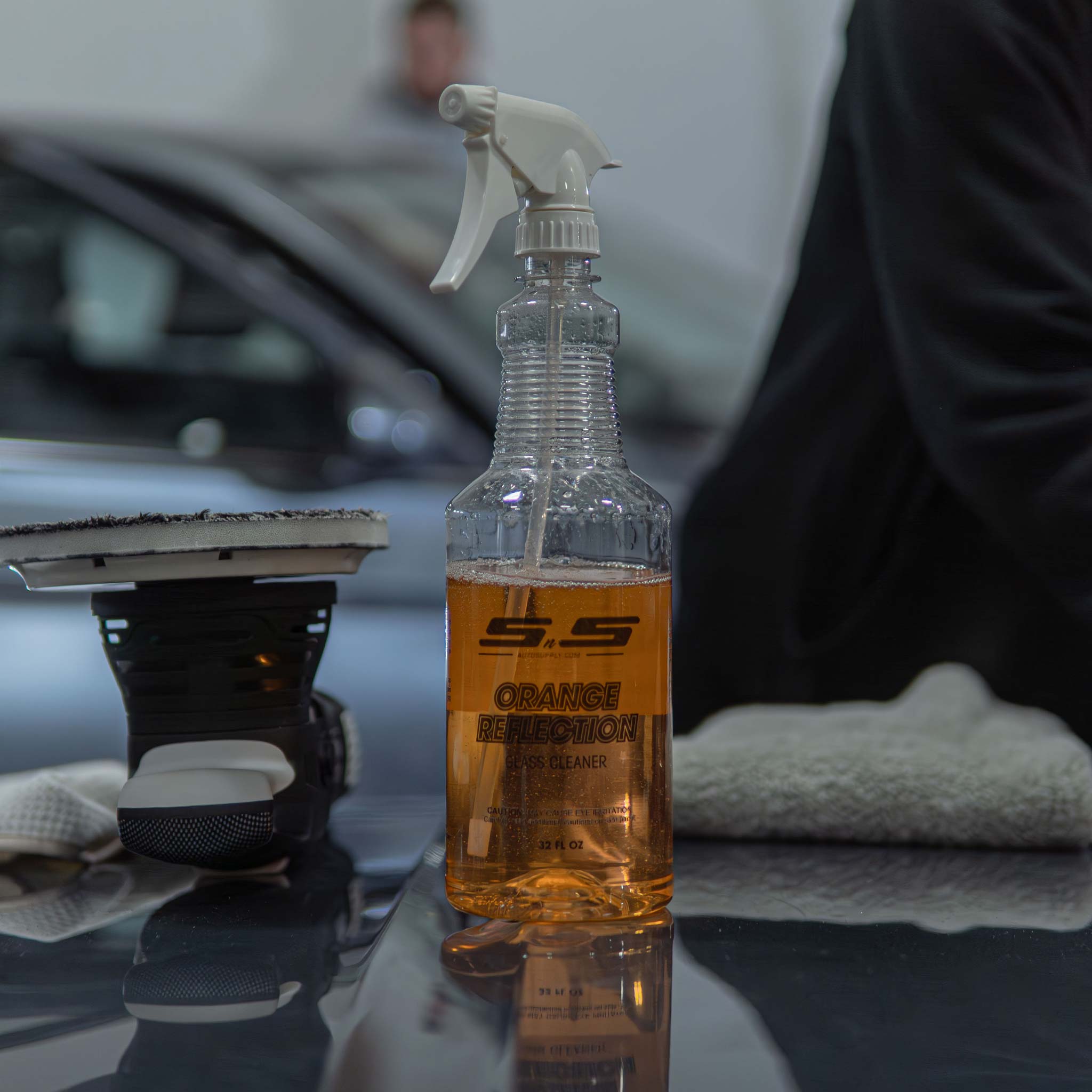 orange reflection gel glass cleaner on car hood surface in shop background