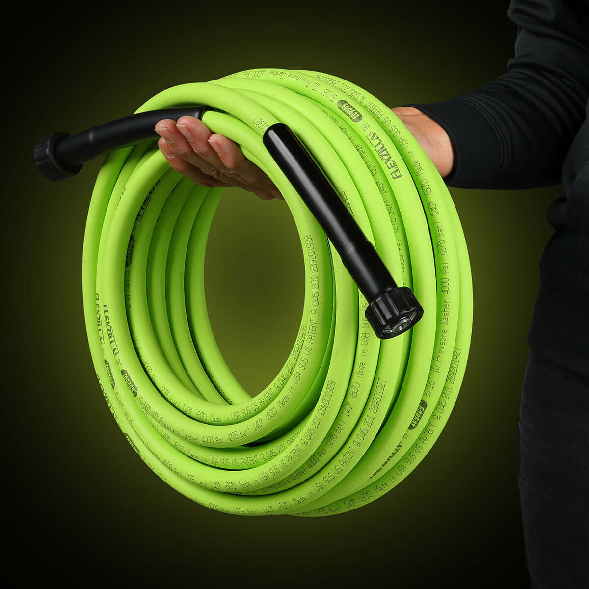 Person holding a coiled flexzilla pressure washer hose with black connectors against a dark background