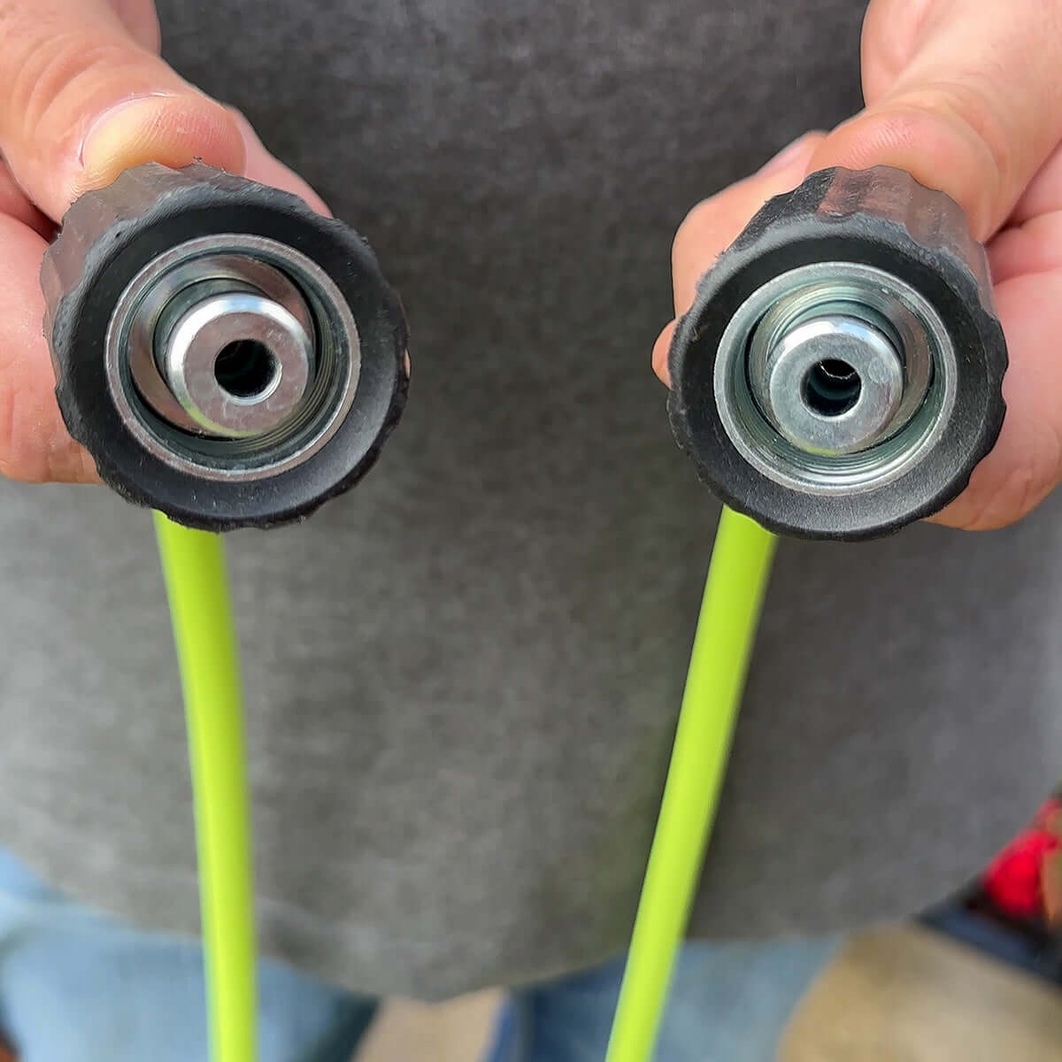 Two green flexzilla connection nozzles held by hands against a gray background