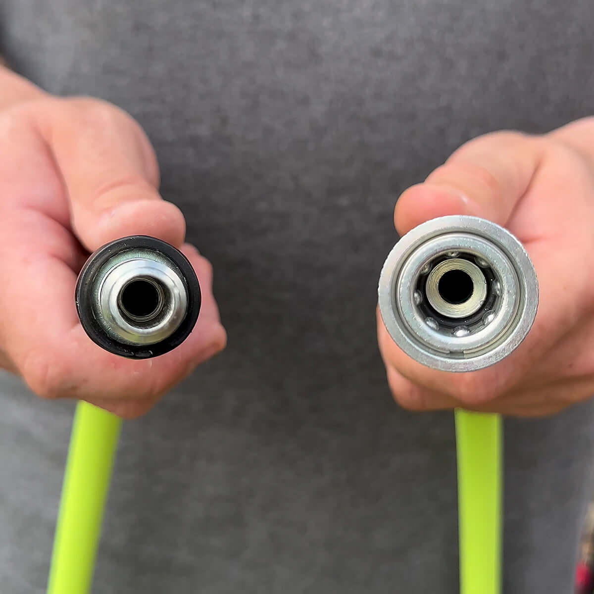 Two hands holding green flexzilla hose with quick connectors against a gray background