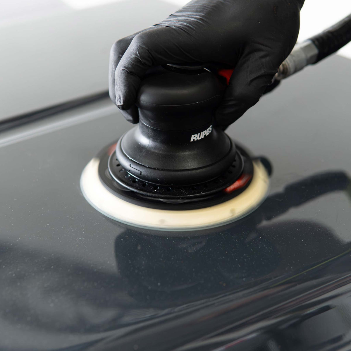 RUPES random orbital sander working a black hood panel during dry sanding
