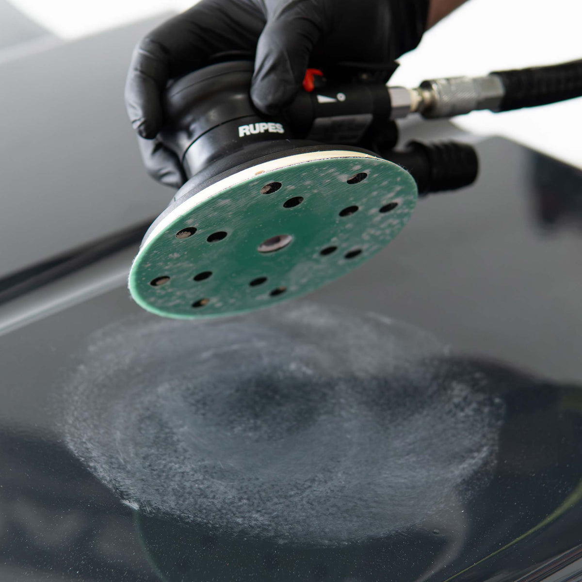 RUPES sander lifted off a black panel showing the sanded scuff pattern in the clear coat