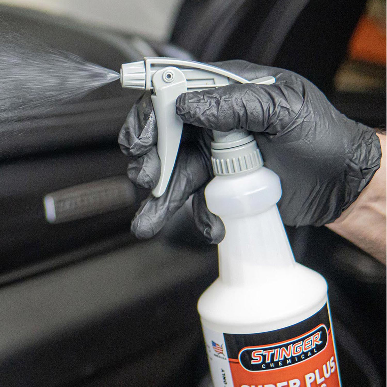 Person wearing gloves using a spray bottle labeled 'Stinger' on a car seat.