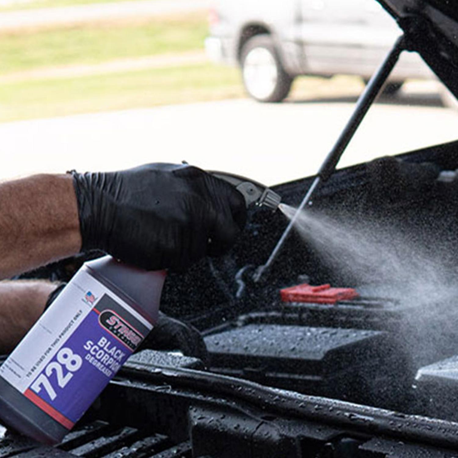 Person cleaning car windshield with a spray bottle labeled '728' in front of a blurred vehicle.